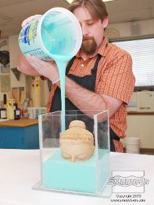 לחיצה להגדלת תמונה שופכים את סיליקון הMold Star® 15 לאט אל תוך אחת מפינות מסגרת התבנית. מניחים לחומר לעלות בעצמו על המודל (במקום לשפוך ישירות על המודל) וכך נמנעים מלכידה של בועות אויר.