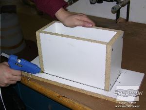 לחיצה להגדלת תמונה מדביקים את קופסת התבנית ללוח העץ בעזרת דבק חם. כך גם אוטמים את הקופסה לדליפה של גומי.