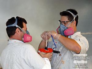 לחיצה להגדלת תמונה העובדים לובשים ציוד מגן מאושר NIOSH הכולל פילטרים לנשימה וכפפות. העובדים מחברים את לחץ האוויר לאקדח הריסוס EZ-Spray Jr.